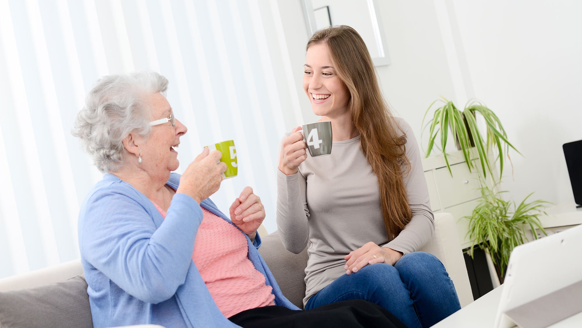 Ältere und jüngere Frau lächeln sich beim Kaffeetrinken an