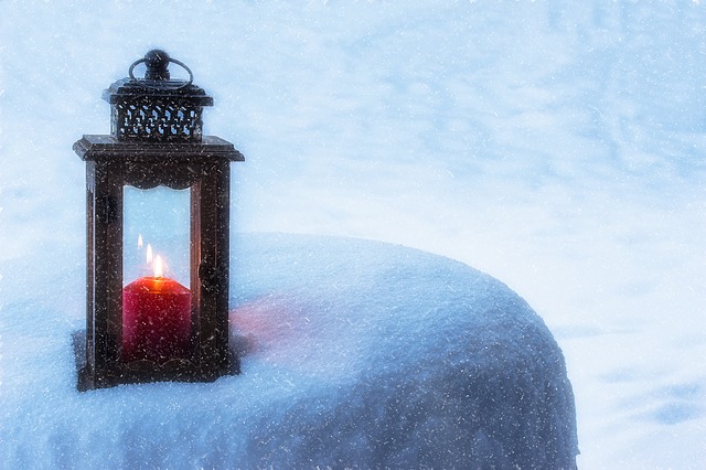 Laterne mit Kerze, die auf einer Schneebedeckten Erhöhung steht.
