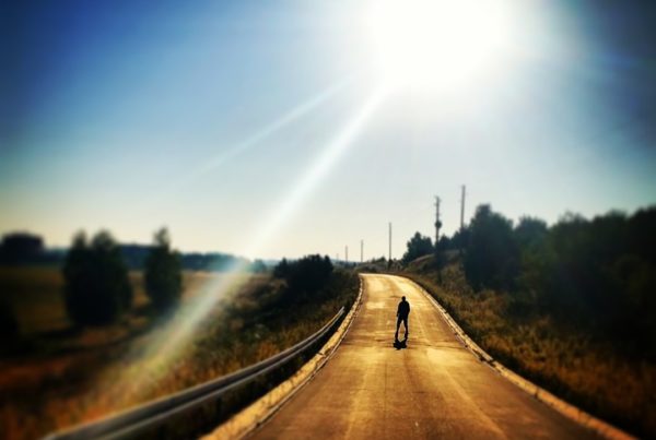 Straße mitten in der Landschaft. auf der eine Person steht. Sonne scheint stark.