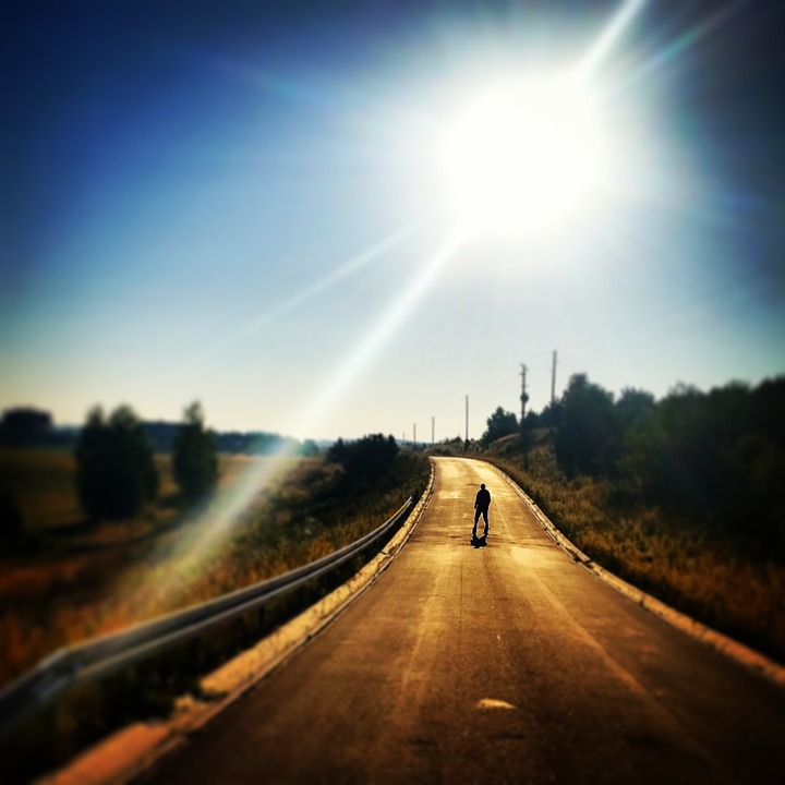 Straße mitten in der Landschaft. auf der eine Person steht. Sonne scheint stark.